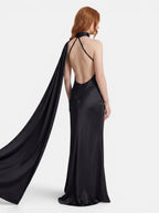 Venatte black satin style halter party dress with backless silhouette and flowing cape detail.